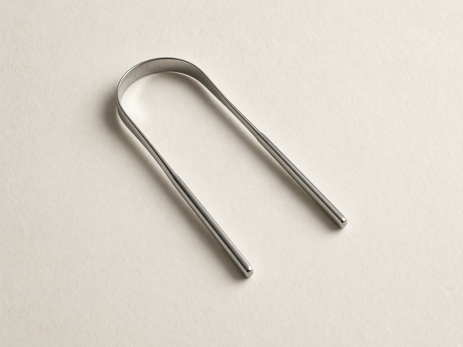 Stainless steel U-shaped tongue scraper on cream archival paper
